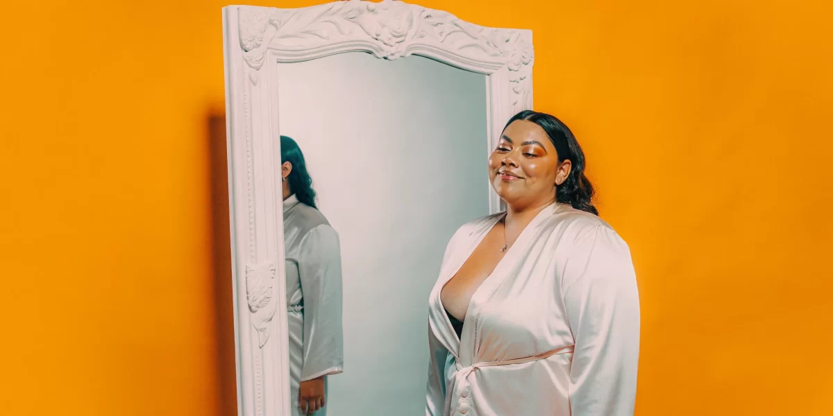 Woman in a satin robe posing for her boudoir session with a male photographer.