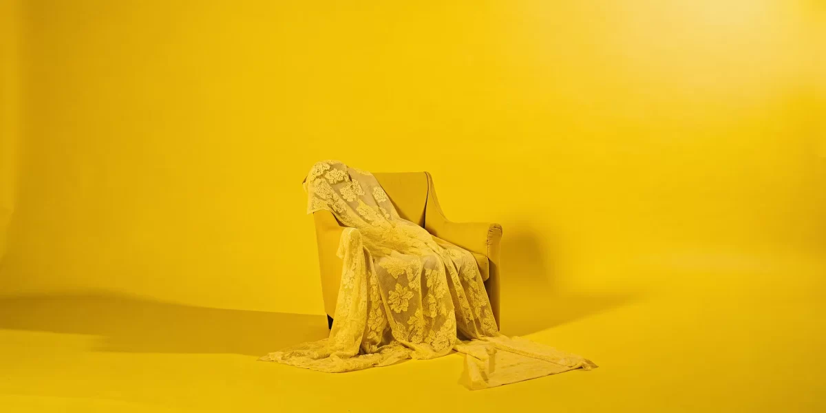 Yellow armchair draped with sheer lace fabric in a bright, high key boudoir scene.