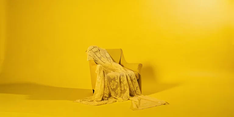 Yellow armchair draped with sheer lace fabric in a bright, high key boudoir scene.